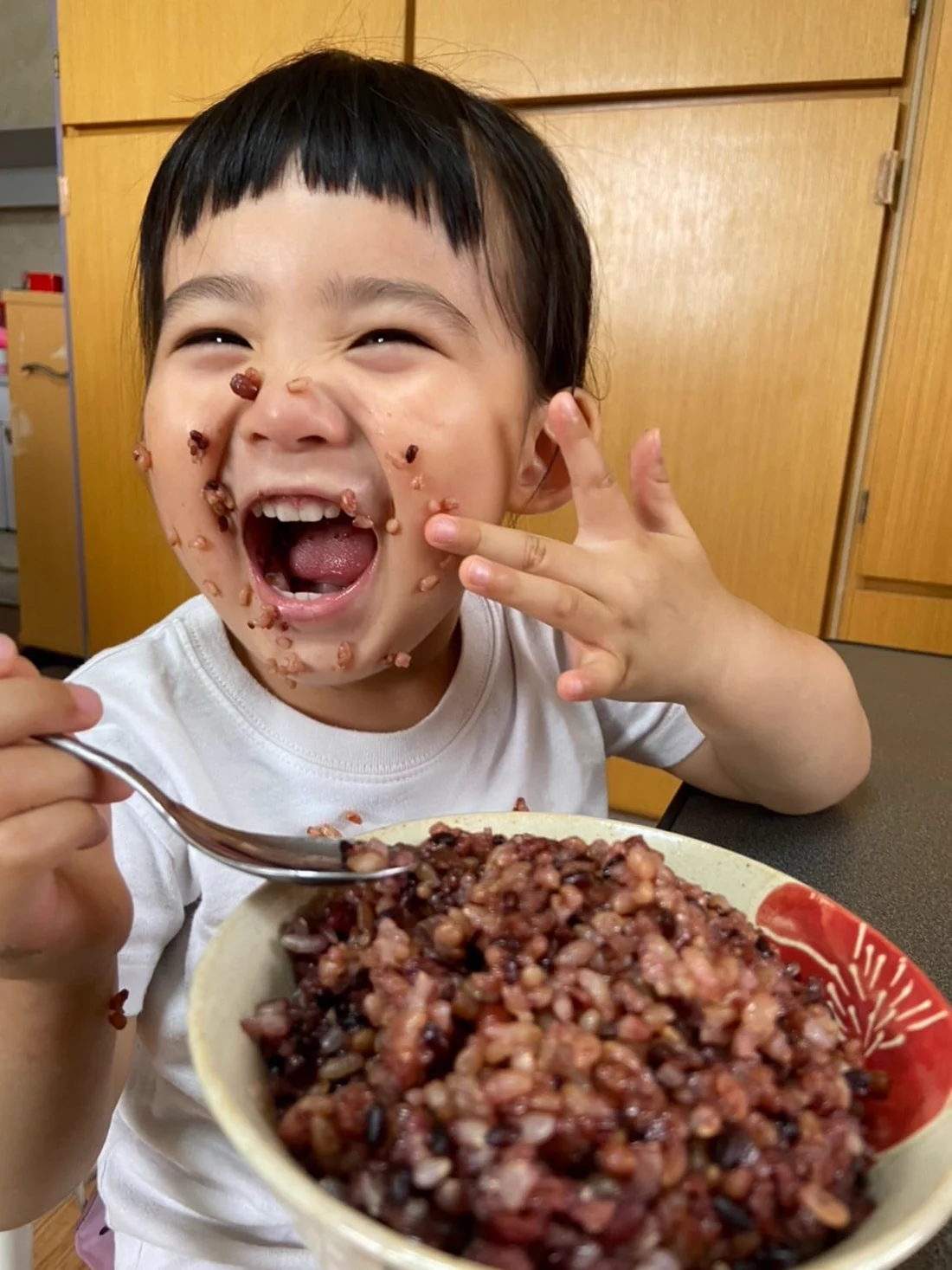 喝米を口いっぱいに頬張って笑う子ども。顔にお米の粒がついている