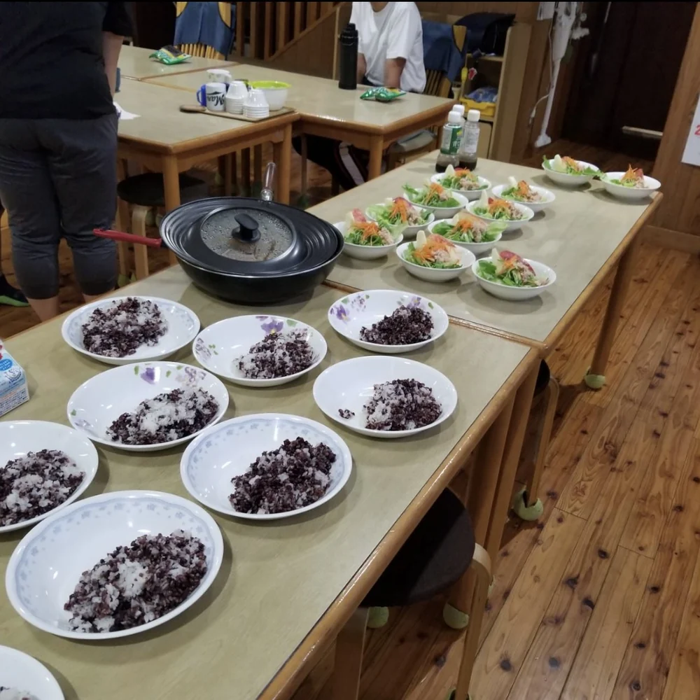学園の配膳台に、喝米ごはんの皿とサラダが並んでいる